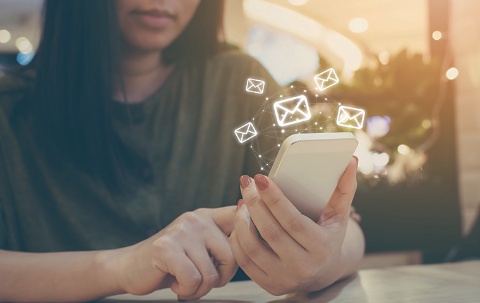 Frau am Handy, vom Handy gehen symbolisch E-Mail-Zeichen ab.