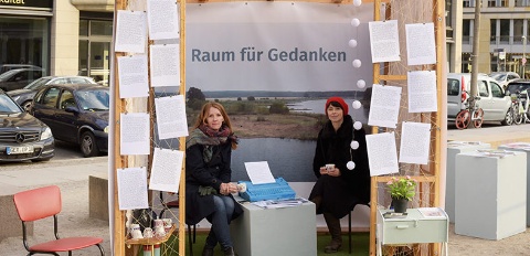 2 Frauen sitzen in einem selbstgebauten kleinen Bungalow mit durchsichtigen Wänden, eingerichtet wie ein Wohnzimmer.