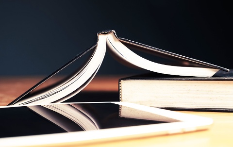 ein Tablet, ein geschlossenes Buch und ein geöffnetes Buch liegen auf einem Tisch